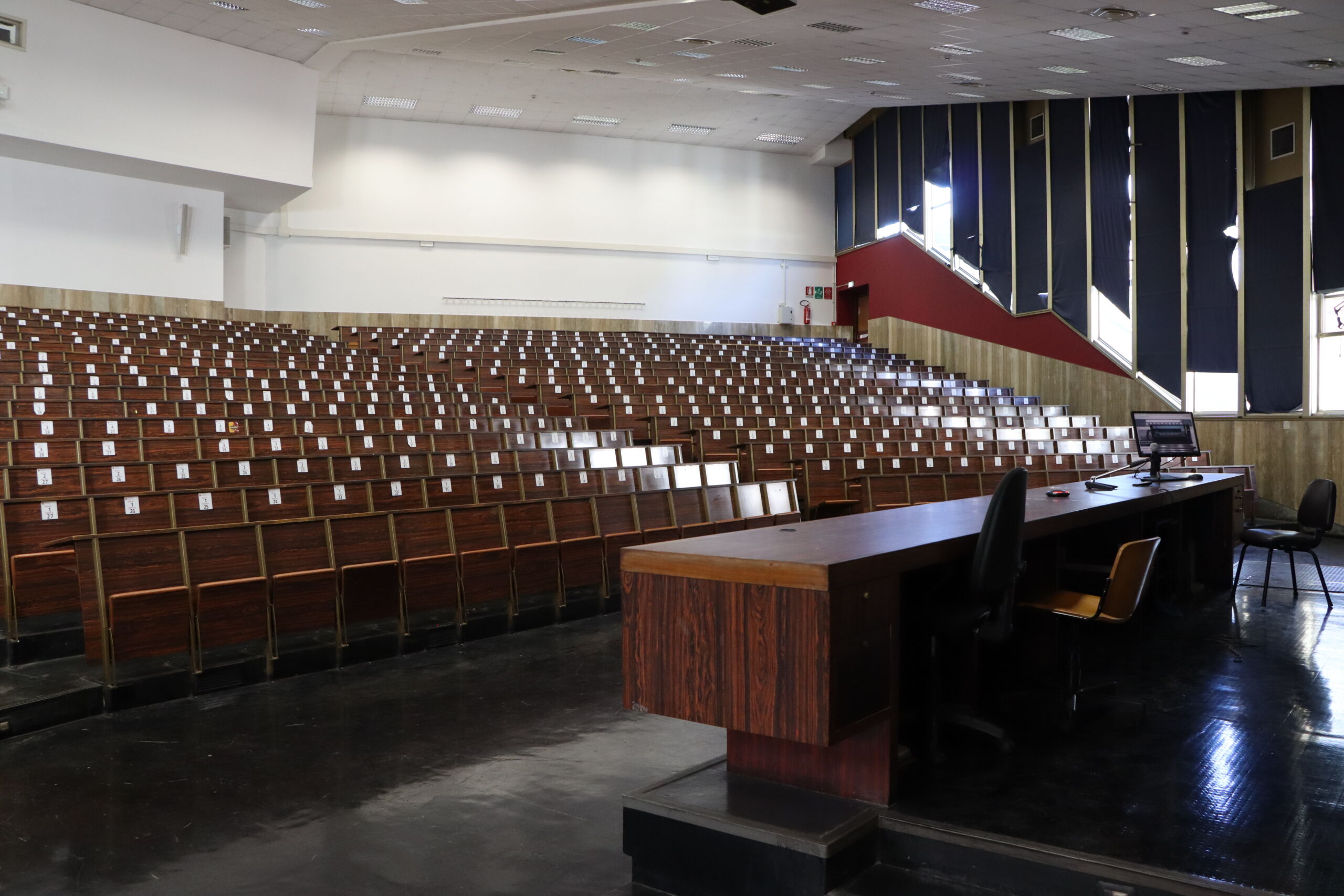 Empty lecture hall with rows of wooden seating and a podium at the front