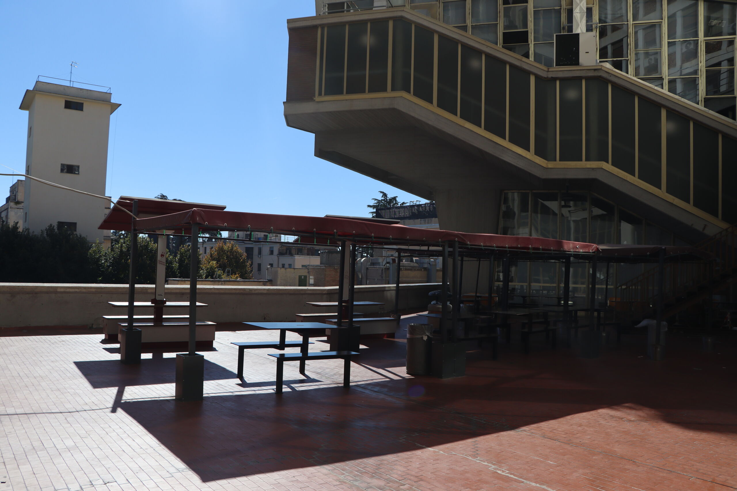 Outdoor terrace with shaded picnic tables beside a modern university building